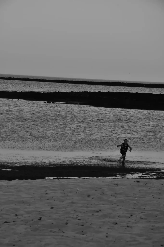 Un jeune garçon sort de l'eau en courant. Photo en Noir et Blanc