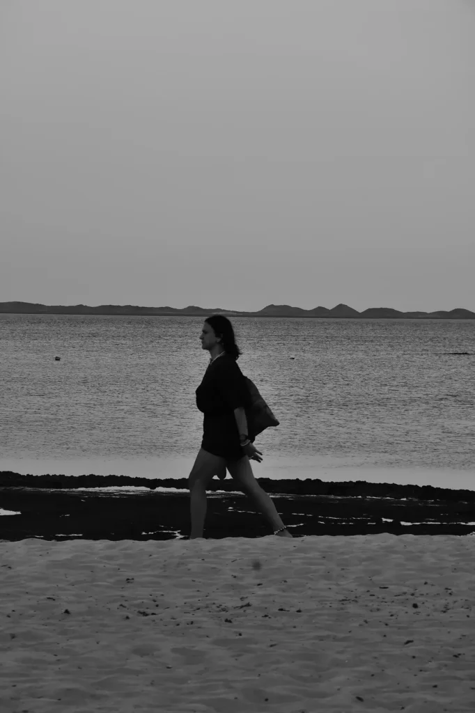 en Noir et Blanc avec une personne qui marche au second plan sur la plage au bord de l'océan