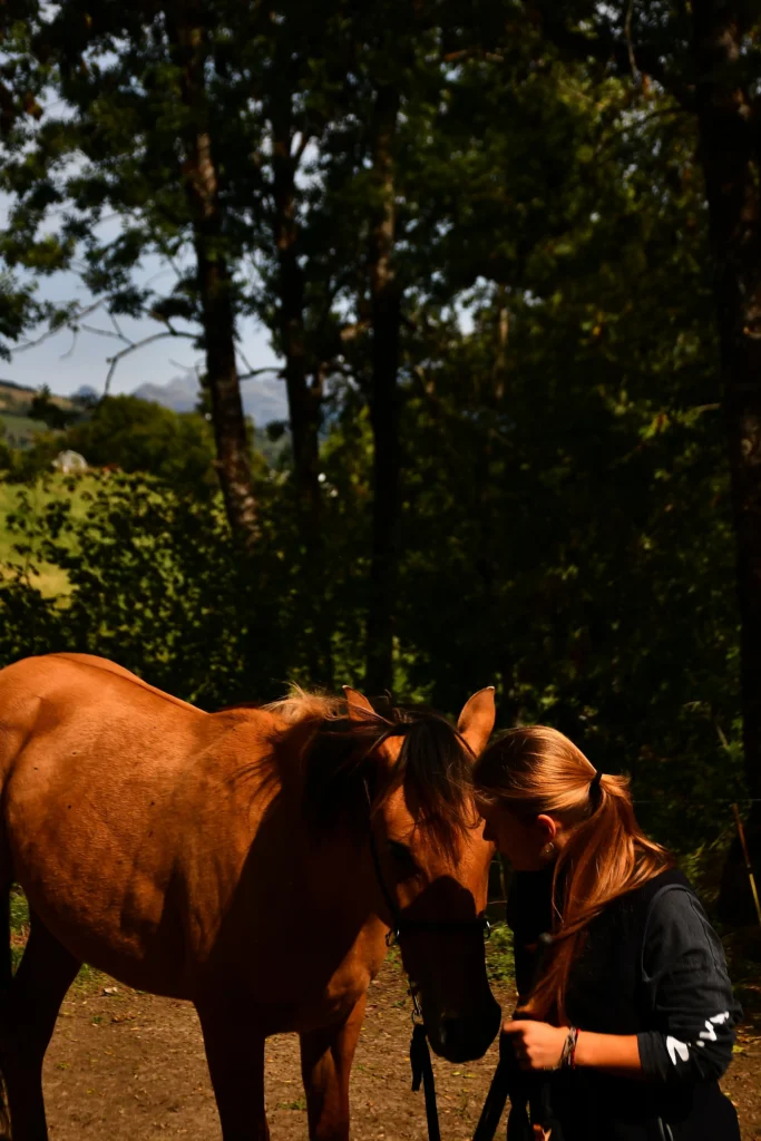 Au premier plan un cheval tenu en longe par une jeune femme avec la forêt au second plan