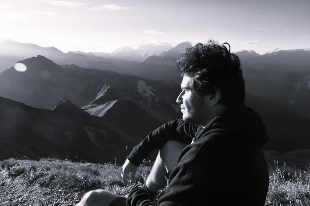 Jeune homme assis au sommet d'une montagne lors d'un lever de soleil