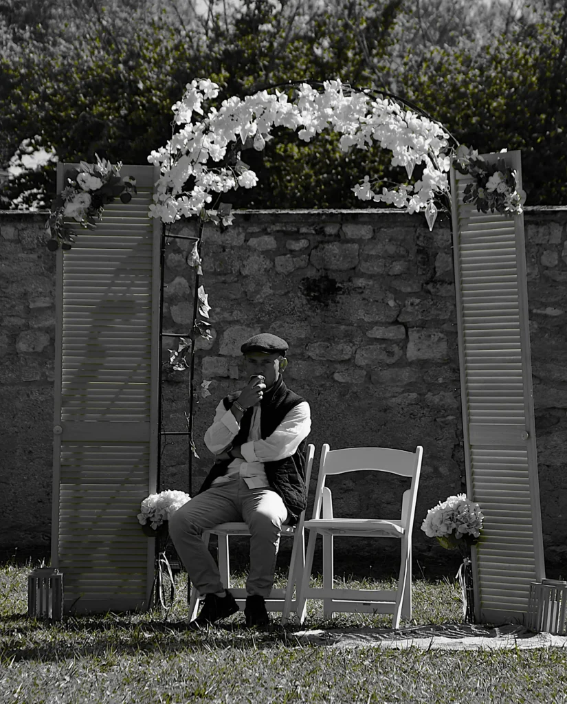 Homme assis lors d'un mariage sur une chaise, casquette sur la tête et café à la main