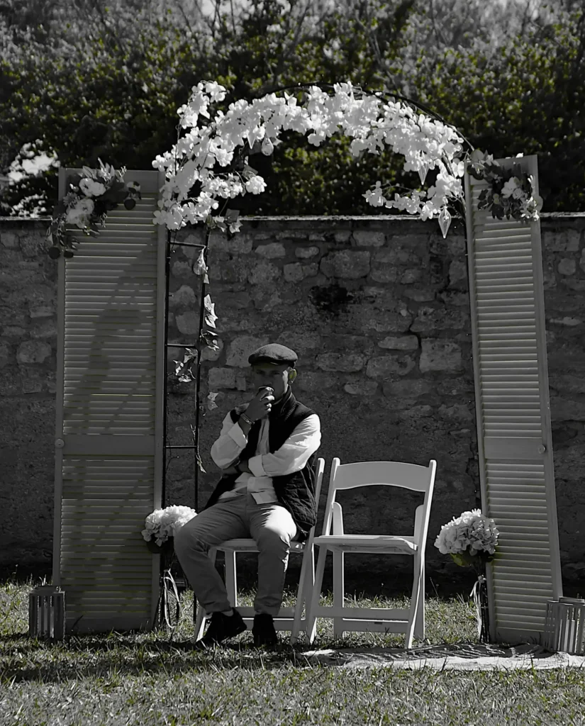 Homme assis lors d'un mariage sur une chaise, casquette sur la tête et café à la main