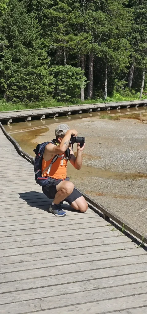 Alexis photographe au bord du lac de La Rosière à Courchevel, sac à dos sur le dos, accroupi pour prendre sa photo