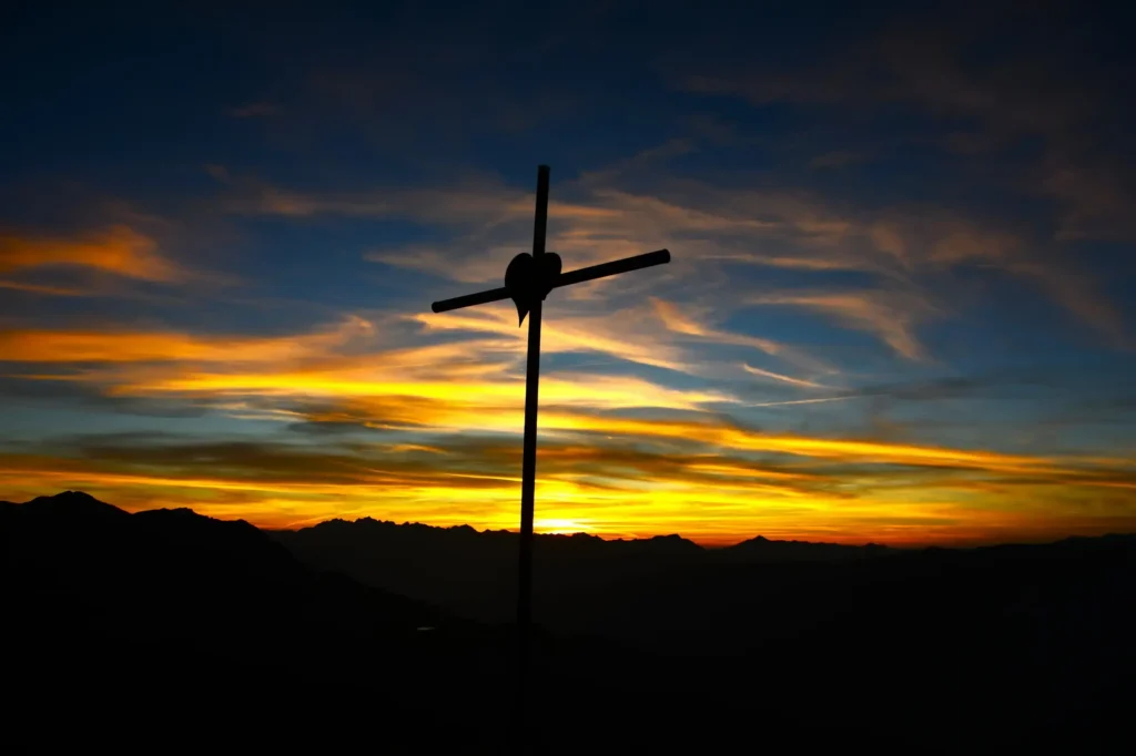 coucher de soleil au sommet d'une montagne avec une croix surmontée d'un coeur au centre