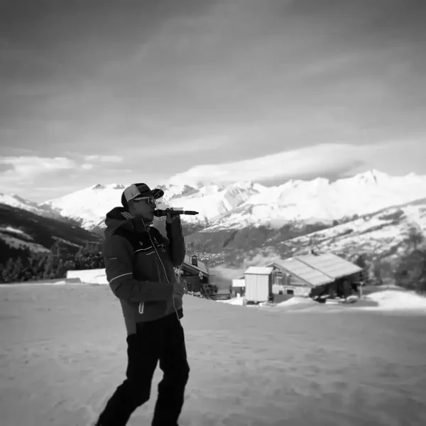 Alexis au micro sur un bord de piste de ski avec une casquette, un manteau d'hiver et son micro porté à la bouche